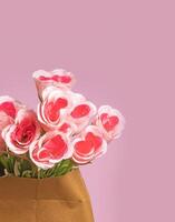 boeket van kunstmatig roze rozen in een bruin papier zak Aan een roze achtergrond foto