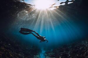 vrij duiker vrouw met vinnen glijdt over- koraal bodem en verbazingwekkend zon stralen. gratis duiken onderwater- in zee foto