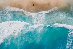 surfer wandelen Aan strand met blauw oceaan en golven. antenne visie foto