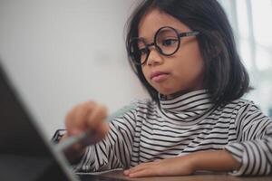 schattig Aziatisch weinig meisje kinderen gebruik makend van een laptop computer, aan het studeren door een online e-learning systeem. foto