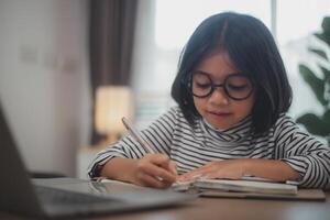 schattig Aziatisch weinig meisje kinderen gebruik makend van een laptop computer, aan het studeren door een online e-learning systeem. foto