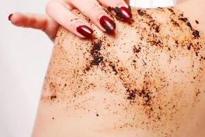 brunette vrouw reinigt de huid van de lichaam koffie schrobben foto