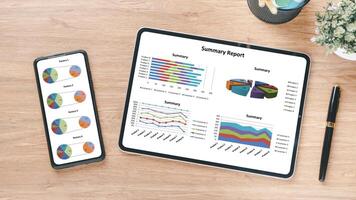 bedrijf analytics concept, overhead visie van een digitaal tablet en smartphone weergeven kleurrijk bedrijf analytics grafieken en een samenvatting verslag doen van Aan een houten bureau. foto