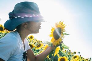 vrouw met hoed zoenen een zonnebloem fabriek geven het de zon foto