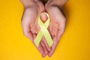 goud lint voor kinderen net zo een symbool van kinderjaren kanker bewustzijn. geel lint Aan hand- foto