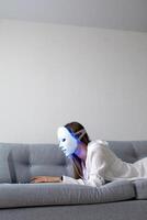 een mooi meisje met een LED masker Aan haar hoofd werken Bij huis Aan een laptop. huis huid zorg concept. foto