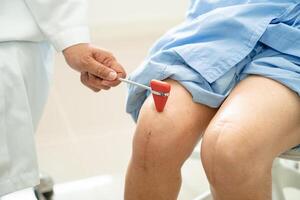 Aziatisch dokter gebruik hamer klop senior vrouw geduldig naar controleren knie reflexen, zenuw en spier in ziekenhuis. foto