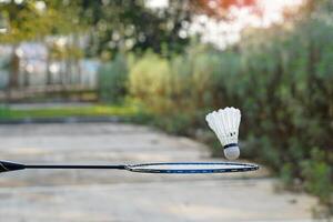 hand- Holding een badminton racket naar vangst een vallend wit shuttle. concept, spelen badminton buitenshuis, vrij val, zwaartekracht, sport, recreatie. foto