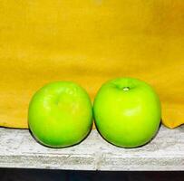 twee groen appels zitten Aan een houten plank foto