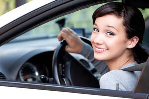 gelukkig eigenaar van een nieuw auto. mooi vrouw bestuurder glimlachen naar u van haar auto- foto