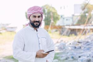 Arabisch Islam moslim volwassen mannetje van saudi Arabië portret gelukkig glimlach staand buitenshuis met slim telefoon foto