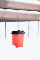 heet koffie in een rood papier kop Aan de sneeuw buiten gedurende een sneeuwval, detailopname foto