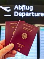 een hand- houdt twee Duitse paspoorten in voorkant van een zacht reizen luchthaven achtergrond Aan vakantie. foto