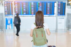 jong vrouw met zak en bagage op zoek naar vlucht tijd informatie bord in Internationale luchthaven, voordat controleren in. reis, vakantie, reis en vervoer concept foto