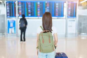 jong vrouw met zak en bagage op zoek naar vlucht tijd informatie bord in Internationale luchthaven, voordat controleren in. reis, vakantie, reis en vervoer concept foto