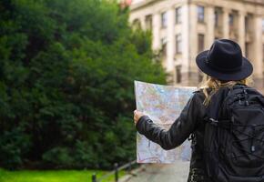 jong meisje is op zoek Bij een stad kaart Aan de straat Aan een reis. vrouw heeft blond haar- vervelend een leer jasje, hoed en rugzak.nieuw reizen concept in nieuw werkelijkheden. hoog kwaliteit foto