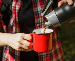 toerist handen gieten koffie van een thermosfles in een metaal rood kopje.selectief focus. achtergrond vervaagd. hoog kwaliteit foto