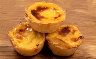 pastel de nata taartjes of Portugees ei scherp Aan een houten bruin achtergrond. pastel de belem is een klein taart met een krokant bladerdeeg gebakje korst en een vla room vulling. zoet nagerecht. foto