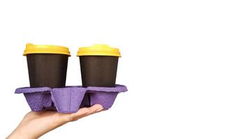 vrouw hand- Holding en portie twee beschikbaar cups van koffie Aan een wit achtergrond met kopiëren ruimte in de studio. ontbijt Aan de Gaan. papier bril met heet drankjes in zwart en geel plastic deksels. foto