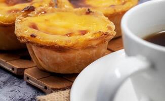 veel van desserts pastel de nata of Portugees ei scherp met een wit kop van zwart koffie. pastel de bel is een klein taart met een krokant bladerdeeg gebakje korst en een vla room vulling. foto