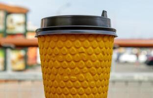 een geel papier glas van thee of koffie - meenemen voedsel Aan een tafel in een cafe. niemand. een beschikbaar glas met een heet drinken staat tegen de backdrop van een zomer cafe. foto