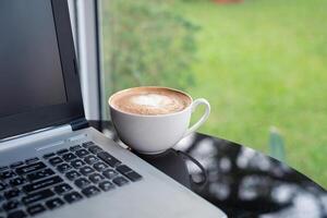 heet latte koffie met modern laptop Aan glas tafel foto