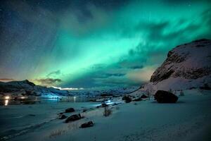 Aurora borealis gloeiend over- besneeuwd berg Aan kustlijn in winter Bij lofoten eilanden foto