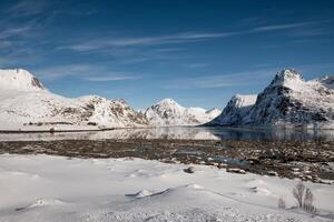 besneeuwd berg reeks met meer Aan kustlijn in zonnig foto