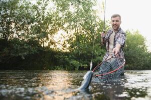 visser vangsten een forel Aan de rivier- in zomer foto