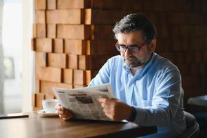 actief senior Mens lezing krant- en drinken koffie in restaurant foto