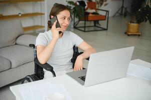 vrouw freelance programmeur zittend in rolstoel en gebruik makend van computers terwijl codering web spel Bij huis. foto