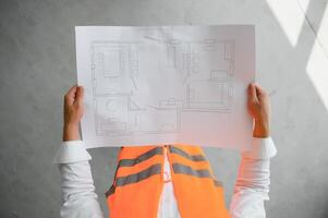 portret van een architect bouwer aan het studeren lay-out plan van de kamers, echt civiel ingenieur werken met documenten Aan bouw plaats, gebouw en huis vernieuwing, professioneel voorman Bij werk. foto