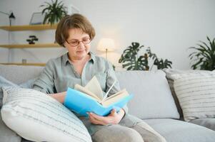 oud dame zittend Aan bankstel en genieten van interessant roman voorraad foto