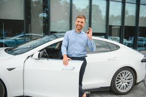 knap jong zakenman staand in de buurt zijn auto buitenshuis. foto