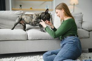 mooi meisje, glimlachen en zittend Aan verdieping in de buurt Frans bulldog foto