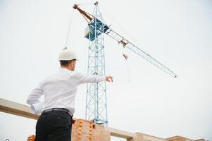 bouw ingenieur toezien op vooruitgang van bouw project staan Aan nieuw beton verdieping top dak en kraan achtergrond. foto