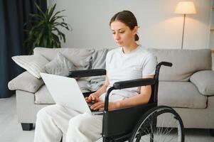 vrouw in een rolstoel werken Aan de laptop pc in de huis kantoor met een bijstand hond net zo een metgezel foto