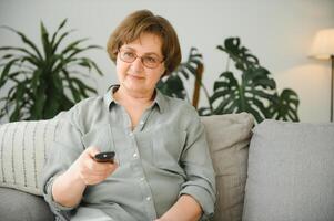 technologie, televisie, leeftijd en mensen concept - gelukkig senior vrouw aan het kijken TV en veranderen kanaal met afgelegen controle Bij huis foto