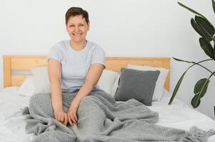 aantrekkelijk midden- oud vrouw ontwaken omhoog in bed. foto