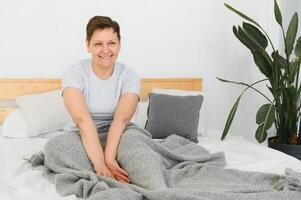 gelukkig vers mooi volwassen ouder vrouw wakker na gezond slaap rekken wakker worden omhoog in knus comfortabel bed, glimlachen midden- oud dame genieten mooi zo ochtend- op zoek Bij camera, dichtbij omhoog portret, top visie. foto