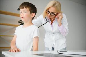 kinderarts luisteren naar ademen in de longen en hartslag met stethoscoop. portret van aanbiddelijk weinig jongen bezoekende dokter. foto