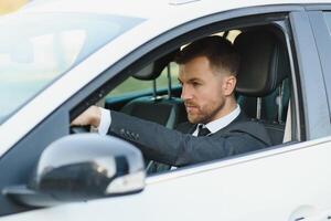 altijd in een haast je. knap jong Mens in vol pak glimlachen terwijl het rijden een auto. foto