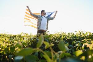 een jong boer staat met een Verenigde Staten van Amerika vlag in een soja veld. de concept van de ons agrarisch industrie. foto