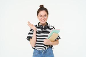 portret van meisje in bril, met hoofdtelefoons over- haar nek, houdt notebooks en studie materiaal voor Universiteit of middelbare school, looks gelukkig en verrast, wit achtergrond foto