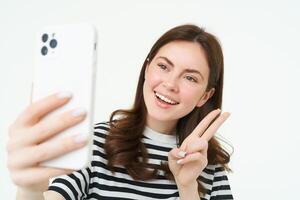 portret van jong vrouw nemen selfies Aan smartphone, poseren voor foto,. gebruik makend van mobiel telefoon app voor nemen grappig en schattig afbeeldingen, geïsoleerd Aan wit achtergrond foto