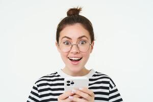 beeld van jong vrouw in bril, gebruik makend van haar mobiel telefoon, staand met smartphone en lachend, staand over- wit achtergrond foto