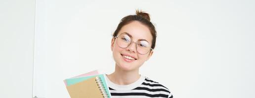 portret van jong vrouw, tutor in bril, Holding haar notebooks en documenten, glimlachen Bij camera, staand over- wit achtergrond foto