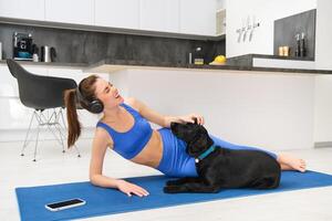 levensstijl en geschiktheid concept. gelukkig jong vrouw aan het doen aerobics terwijl haar hond wil naar Speel, lachend en lachend, houdende Aan yoga mat foto