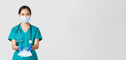 covid19, coronavirus ziekte, gezondheidszorg arbeiders concept. vriendelijk glimlachen Aziatisch arts, vrouw dokter in scrubs en rubber handschoenen overhandigen over- medisch maskers naar patiënten, wit achtergrond foto