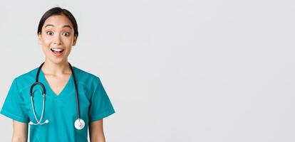 gezondheidszorg arbeiders, voorkomen virus, quarantaine campagne concept. gelukkig en opgewonden Aziatisch vrouw dokter, arts in scrubs kijken versteld staan, horen geweldig nieuws, wit achtergrond foto